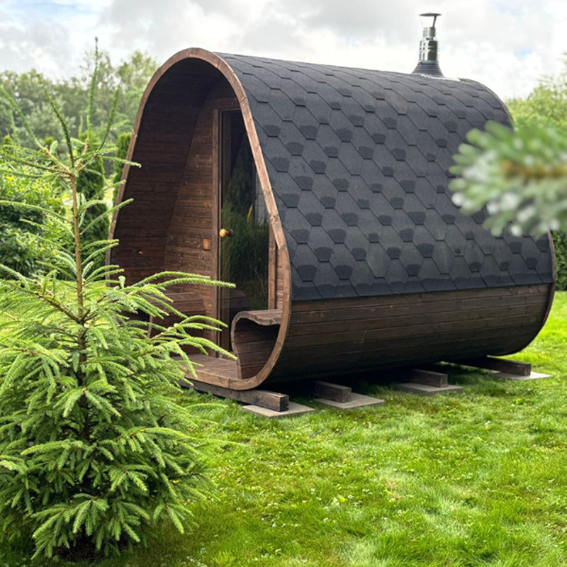 Celsium Herkus Small garden sauna in the garden in summer weather, with elegantly curved roof and black bitumen covering.